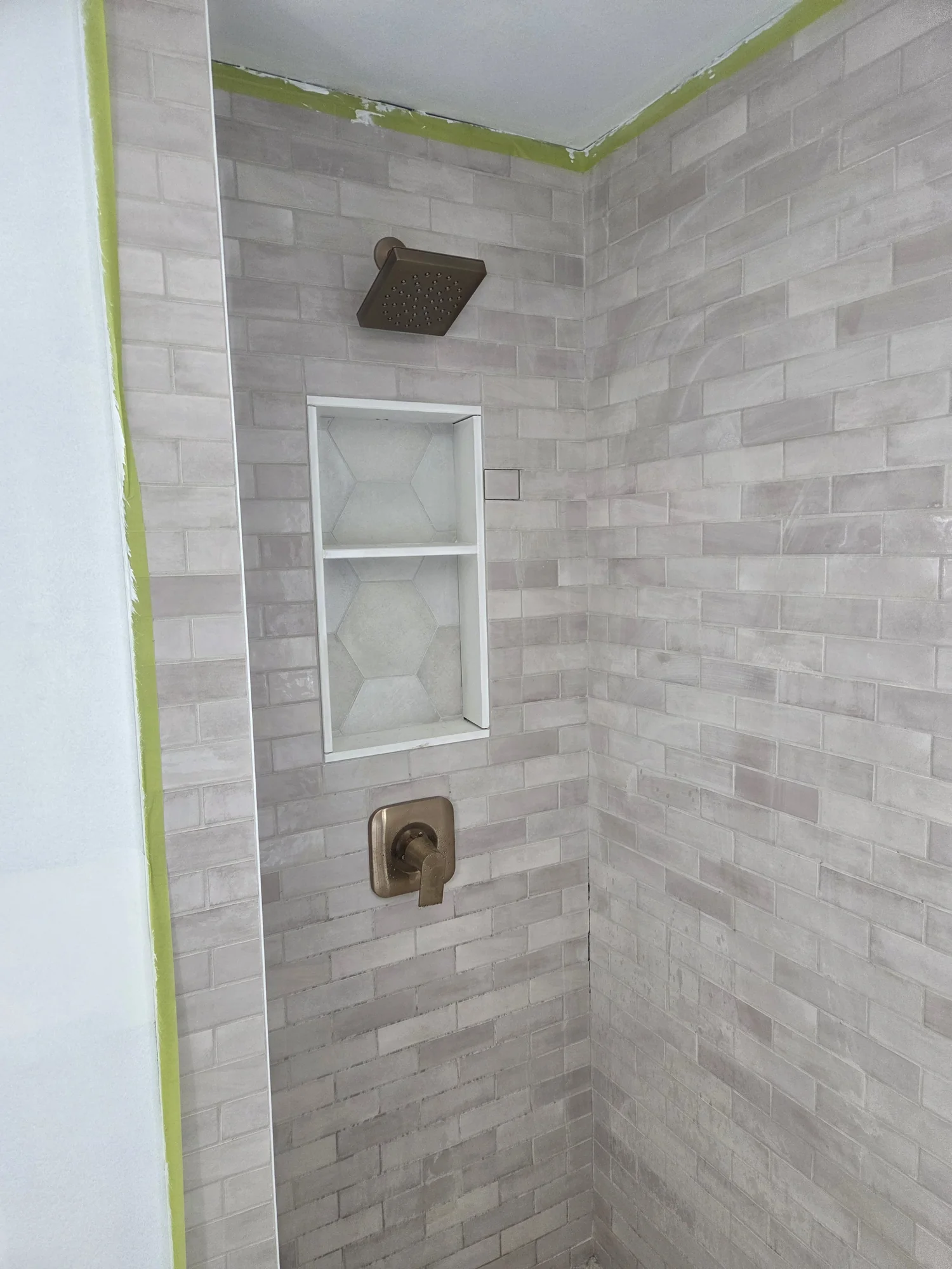 Grey tiled shower with brass controls and a recessed shelf